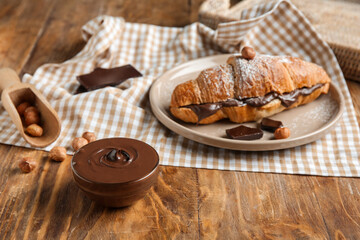 Plate of sweet croissant with chocolate spread and hazelnuts on wooden background