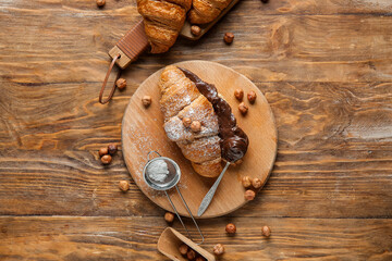 Boards of sweet croissants with chocolate spread and hazelnuts on wooden background