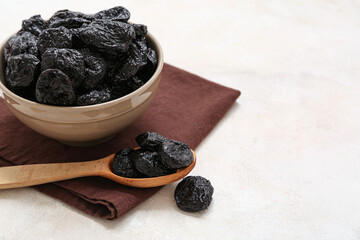 Bowl and wooden spoon with dried prunes on white background