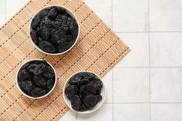 Bowls with dried prunes on white tile background