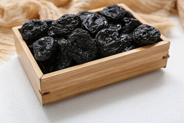 Wooden box with dried prunes on white background