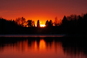 Naklejka premium Sunset colours reflected from a calm lake in spring in Western Finland