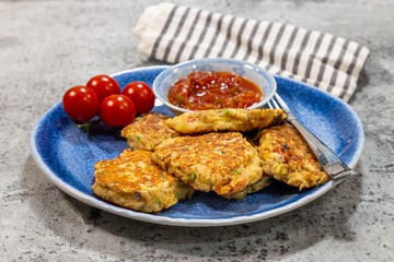 A plate of fried fish fritters with a small dish of salsa for dipping and cherry tomatoes for decoration on a restaurant table