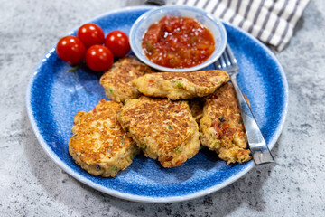 A plate of fried fish fritters with a small dish of salsa for dipping and cherry tomatoes for decoration