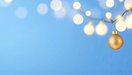 Golden ornament hanging against a soft blue background with blurred festive lights