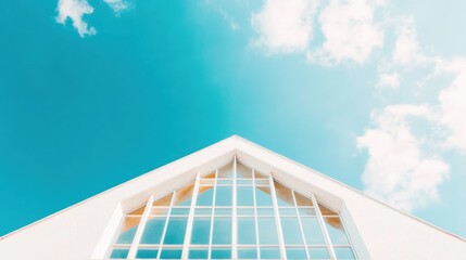 The striking, symmetrical roof structure stands out against the clear blue sky, framed by soft white clouds, inciting a sense of architectural beauty
