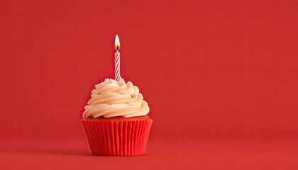 A vibrant red cupcake with creamy frosting and a lit candle set against a solid red background