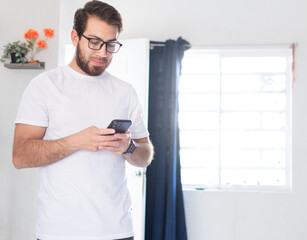Hombre soltero en casa, usando el teléfono celular. Joven apuesto escribiendo un mensaje