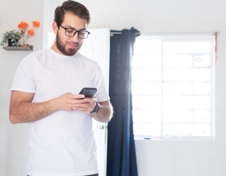 Hombre soltero en casa, usando el tel&eacute;fono celular. Joven apuesto escribiendo un mensaje