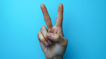 Naklejka premium Close-up of a hand showing the peace sign against a vibrant blue backdrop. A minimalist image with a symbolic gesture.