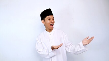 excited handsome young asian muslim man looking and showing his hand recommending something on the side isolated on white background