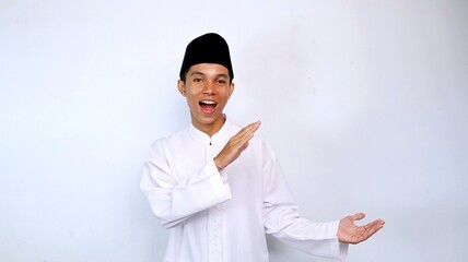 excited handsome young asian muslim man showing his hand recommending something on the side isolated on white background