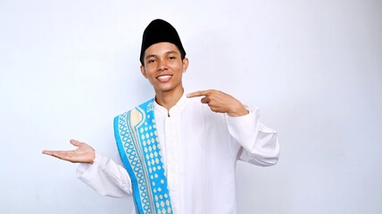 handsome asian muslim young man smiling pose pointing palm promotion, product and discount on the side. recommend something with isolated white background