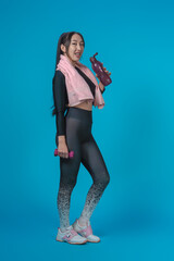 Slim Asian girl in sportswear with a towel around her neck and a bottle of water after a workout. Isolated blue background. Healthy lifestyle concept