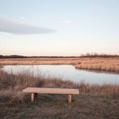 Obraz premium Tranquil Scenic View of a Wooden Bench by a Serene Grassland Lake at Dusk Under a Soft Sky with Gentle Clouds and Golden Sunrise Reflections