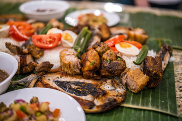 Traditional feast featuring grilled fish, chicken, rice, and fresh vegetables served on banana leaves