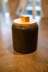 Unique black jar with wooden lid on a textured wooden table in a modern interior setting
