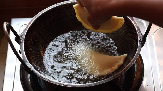 Delicious Bengali beef puli pitha being prepared and fried in oil in a karahi on a gas stove. Puli Pitha is a popular traditional Bengali dish.