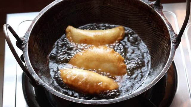 Delicious Bengali beef puli pitha frying in a karahi on a kitchen gas stove. Puli Pitha is a traditional Bengali dish.