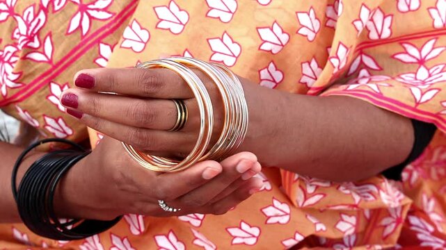 Close-up of a Bengali woman's hand adorned with glass bangles, a ring, and nail polish.