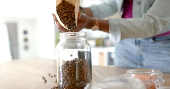 Pouring coffee beans into glass jar, woman preparing fresh coffee at home