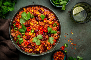 Chili con carne with minced beef, beans, paprika, corn, cilantro, jalapeno pepper in tomato sauce, tex-mex cuisine in green frying pan, top view