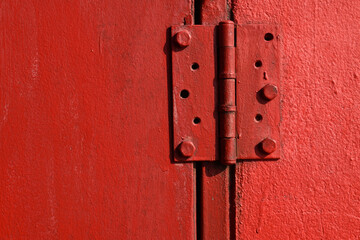 steel hinge painted vibrant red on grunge door under sunlight with shadow