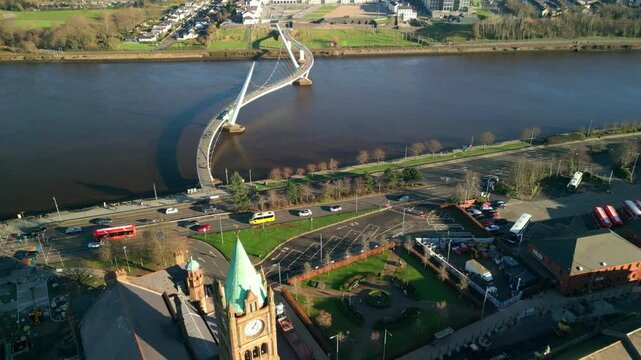 High, forward travelling aerial shot of the Peace Bridge, the Guildhall and the River Foyle in Derry-Londonderry, NI on a bright and sunny day. Filmed in 4K at 60fps and in Rec709 color space.