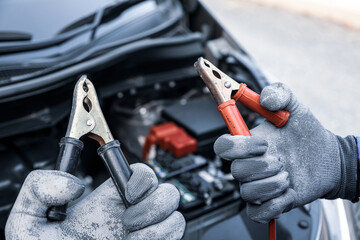 Car mechanic holding connect jumper cable or car booster cables on terminal dead battery for...