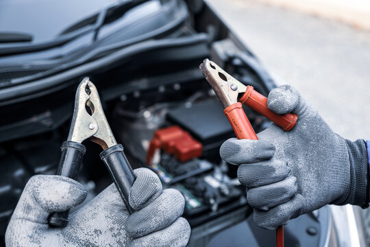 Car mechanic holding connect jumper cable or car booster cables on terminal dead battery for jump-start or check car battery fail problem change repairing and fix car with maintenance service.