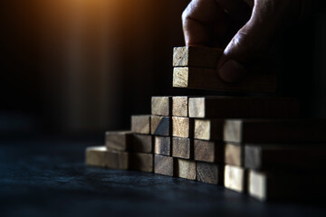 Hand place wooden block stack in pyramid stair step concept team building of prevent not collapse...