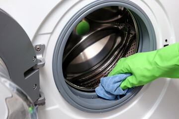 A woman's hand in a protective rubber glove wipes away moisture a washing machine.