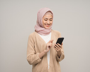 Portrait happy young asian muslim woman holding smartphone standing on isolated white background....
