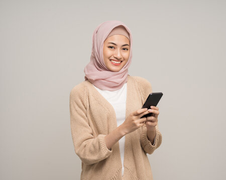 Portrait happy young asian muslim woman holding smartphone standing on isolated white background. Beautiful Attractive Muslim woman wearing abaya and hijab fashion costume shot in studio