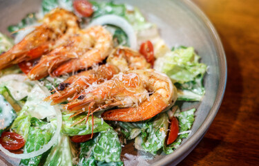 Caesar salad with Fried shrimp in a plate served ready to eat on a wooden table.