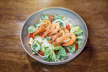 Caesar salad with Fried shrimp in a plate served ready to eat on a wooden table.