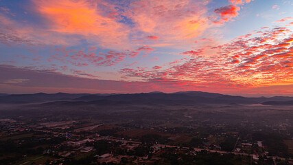 A breathtaking sunrise illuminates a small village nestled among lush green fields and karst mountains, with vibrant clouds filling the sky. The harmony of rural life set dramatic natural formations.