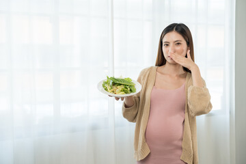 Unhappy young asian pregnant woman feeling with morning sickness to vegetable salad, frustrated...