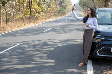 Young woman searching for a mobile network in the forest with her damaged car, bad connection and...