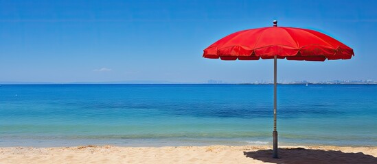 Red beach umbrella on sandy shore with vibrant blue ocean and clear sky in the background creating a serene summer vacation scene.