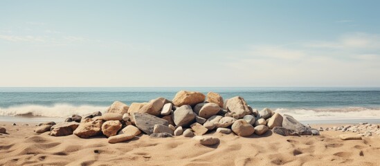 A serene beach scene featuring a pile of smooth stones on a golden sandy shoreline with calm blue ocean waves under a clear sky
