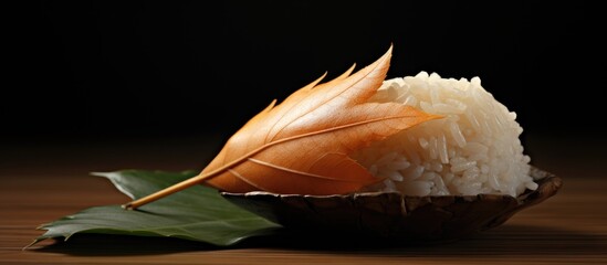 Oak leaf elegantly enfolds a mound of white rice in a dark setting with a wooden surface and green leaf accents creating a serene food composition