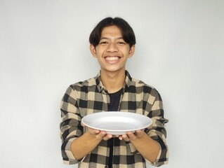 Young Asian man smiling happily while pointing at empty dinner plate