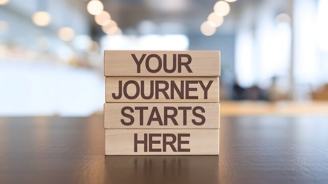 Four wooden blocks stacked on a dark surface read "YOUR JOURNEY STARTS HERE" in serif font. A blurred bright background highlights the clean, motivational message about new beginnings and ventures.



