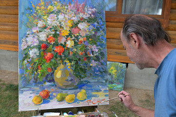 Artist puts his autograph under a still life he has just painted. Selective focus