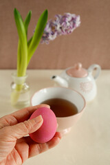 hand holding pink easter egg with spring tea setup
