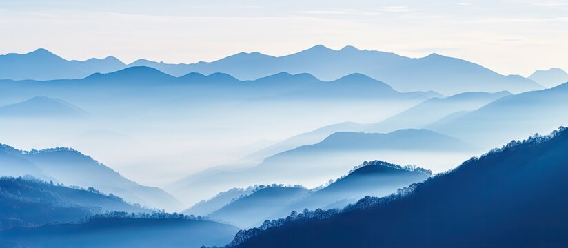 Serene mountain range featuring blue and soft gray silhouettes emerging from colorful morning fog with gentle light illuminating the landscape.
