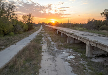 Fototapeta premium A photograph of an abandoned highway overpass at sunset, with cracked concrete and broken bridges, showcasing the urban decay and scale of post-apocalyptic architecture. The scene is captured 