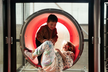 Children Sharing Laughter While Playing Together in a Red Tunnel Slide
