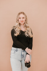 Young female photographer holding a camera against a beige background